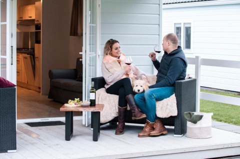 Pareja tomando vino con su perro en el porche del Verandah Chalet, Camping Sevink Molen, Países Bajos.