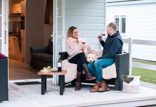 Pareja tomando vino con su perro en el porche del Verandah Chalet, Camping Sevink Molen, Países Bajos.