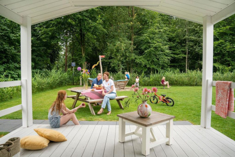 Familia disfruta en el porche y jardín del Verandah Chalet, Camping Sevink Molen en los Países Bajos.
