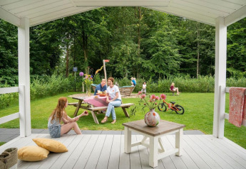 Famiglia si rilassa sulla veranda e nel giardino del Verandah Chalet, Camping Sevink Molen nei Paesi Bassi.