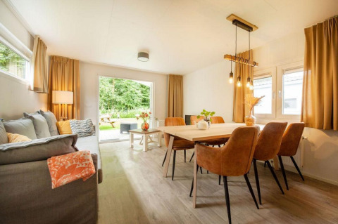 Lys og hyggelig stue med spisebord og sofa i et glampingophold, udsigt til have gennem glasdør.