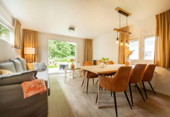 Lys og hyggelig stue med spisebord og sofa i et glampingophold, udsigt til have gennem glasdør.