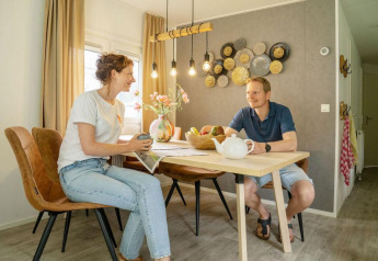 Two people enjoying breakfast at the dining table in Verandah Chalet at Camping Sevink Molen, Netherlands.