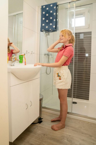 Niña junto al lavabo en el baño del Verandah Chalet en Camping Sevink Molen, Países Bajos.