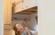 Twee kinderen in een glampingkamer met stapelbedden: het meisje leest beneden, de jongen kijkt lachend toe.