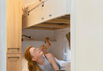 Dos niños disfrutan de una habitación glamping con literas; la niña lee abajo y el niño sonríe arriba.