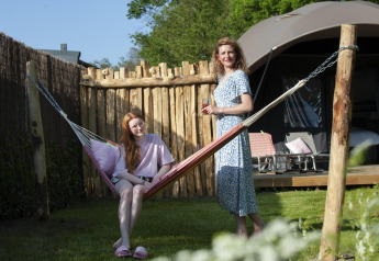 Mother and daughter relaxing by a hammock in front of a lodge at Camping Sevink Molen, Netherlands.