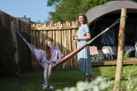 Mor og datter slapper af ved en hængekøje foran en lodge på Camping Sevink Molen, Nederlandene.