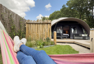 Personne se relaxant dans un hamac devant la Nature Wellness Suite Hot tub au Camping Sevink Molen, Pays-Bas.