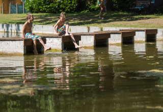 Due bambini siedono su un pontile di legno e giocano con i piedi nell'acqua al Jocomo Parc, Belgio.
