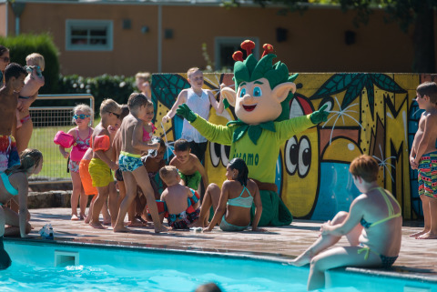 Børn leger ved en pool med en maskot i grøn kostume på Jocomo Parc feriepark i Limburg, Belgien.