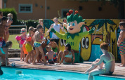 Bambini giocano con una mascotte verde vicino alla piscina al parco vacanze Jocomo Parc in Limburgo, Belgio.