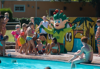Kinderen spelen met een groene mascotte bij het zwembad van Jocomo Parc vakantiepark in Limburg, België.