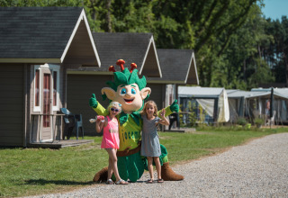Two children pose with a mascot in front of lodges at Jocomo Parc, a holiday park in Limburg, Belgium.