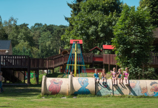 Kinder spielen in Jocomo Parc, Belgien, auf einem bemalten Rohr auf einem grünen Spielplatz.