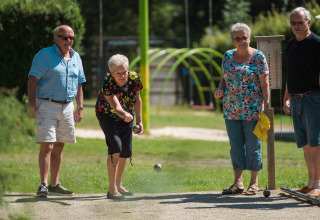 Fire ældre voksne spiller petanque udendørs på en solrig dag i Jocomo Parc, Limburg, Belgien.