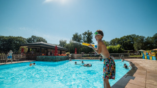 Kinderen spelen bij het zwembad van Jocomo Parc, een vakantiepark in Limburg, België, in de zon.