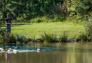 Ragazzo che pesca vicino allo stagno tranquillo di Jocomo Parc, parco vacanze in Limburgo, Belgio.