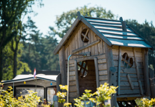 Houten speelhuisje met speelse ramen in Jocomo Parc, Limburg, België, omringd door natuur.