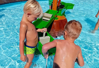 Børn leger med et vandspil i en swimmingpool under solen i Jocomo Parc feriepark i Belgien.