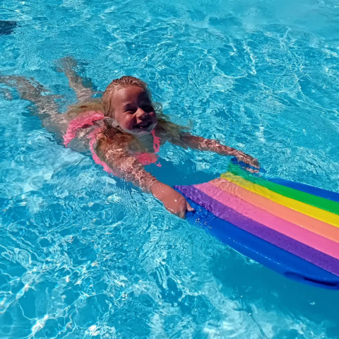 Una niña sonriente nada en la piscina con una tablita colorida en Jocomo Parc, Limburg, Bélgica.