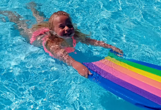 A smiling girl swimming in the pool with a colorful kickboard at Jocomo Parc, Limburg, Belgium.