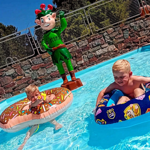 Deux enfants jouent dans une piscine avec des bouées près d'une statue d'elfe vert au Jocomo Parc, Belgique.