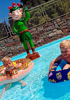 Dos niños juegan en una piscina con flotadores junto a una estatua de elfo verde en Jocomo Parc, Bélgica.