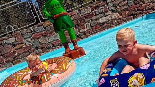 Dos niños juegan en una piscina con flotadores junto a una estatua de elfo verde en Jocomo Parc, Bélgica.