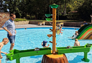 Kinder spielen in einem flachen Kinderbecken mit Wasserspielgeräten im Jocomo Parc, Belgisch-Limburg.