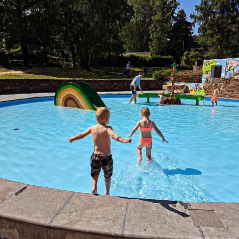 Niños jugando y corriendo hacia una piscina poco profunda en Jocomo Parc, parque de vacaciones en Limburg, Bélgica, en un día soleado.