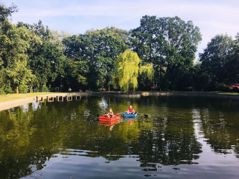 Twee mensen varen met bootjes op het meer in Jocomo Parc, omgeven door groene bomen in Limburg.