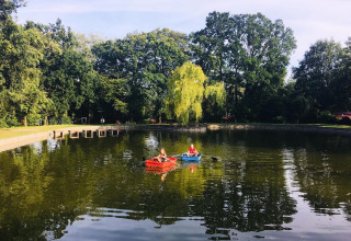 Zwei Personen rudern auf einem ruhigen See im Jocomo Parc, umgeben von grünen Bäumen in Belgien.