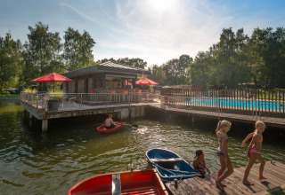 Des enfants jouent près du lac et de la piscine à Jocomo Parc, parc de vacances en Limbourg, Belgique, entourés de nature.