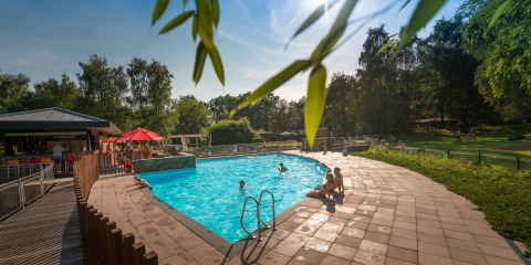 Solrig eftermiddag ved swimmingpoolen på Jocomo Parc feriepark i Limburg, Belgien, omgivet af natur.