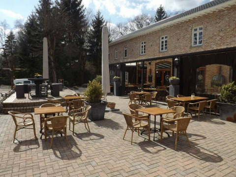 Buitenterras met tafels en stoelen in Jocomo Parc vakantiepark in Belgisch Limburg, omringd door bomen.