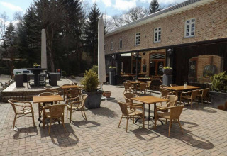 Terrasse extérieure avec tables et chaises au parc de vacances Jocomo Parc en Limbourg belge, entourée d’arbres.