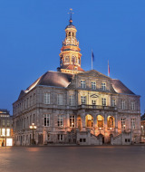 Fachada iluminada de un ayuntamiento histórico en una plaza principal bajo el cielo azul al anochecer.