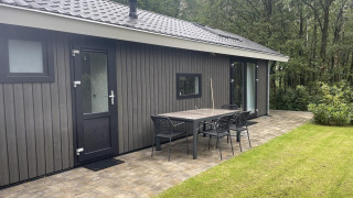 Vista exterior de Bos Cottage en De Thijmse Berg, Países Bajos, con mesa en la terraza y un fondo de bosque.
