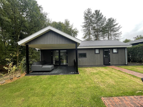 Außenansicht der Bos Cottage Deluxe Lodge im De Thijmse Berg, Niederlande, mit überdachter Terrasse und Sofa.