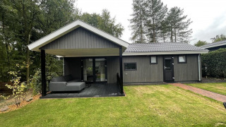 Vista exterior de Bos Cottage Deluxe en De Thijmse Berg, Países Bajos, con terraza cubierta y césped verde.