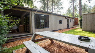 Zona exterior de Boslodge en De Thijmse Berg, Países Bajos, con terraza, banco de madera y vegetación.