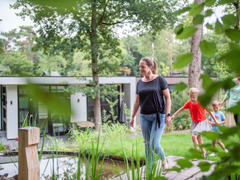Familie spaziert durch einen grünen Garten vor einem modernen Ferienhaus im Recreatiepark Beekbergen.