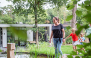 En familie nyder en gåtur gennem den grønne have ved en moderne feriebolig i Recreatiepark Beekbergen.