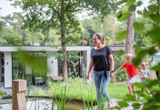 Een gezin wandelt door de groene tuin van een modern vakantiehuis in Recreatiepark Beekbergen.