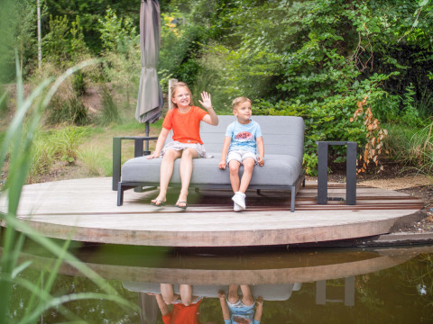 Zwei Kinder sitzen auf einer Bank am Teich im Freizeitpark Beekbergen in Gelderland, Niederlande.