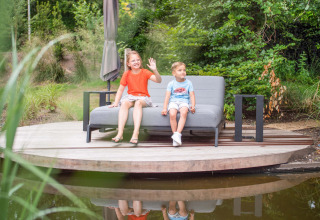 Zwei Kinder sitzen auf einer Bank am Teich im Freizeitpark Beekbergen in Gelderland, Niederlande.