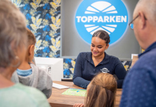 Rezeptionistin begrüßt Familie im Recreatiepark Beekbergen, einem Ferienpark in Gelderland, Niederlande.