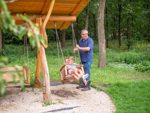 Ein älterer Mann schaukelt zwei Kinder auf einer Holzschaukel im Recreatiepark Beekbergen, Gelderland.