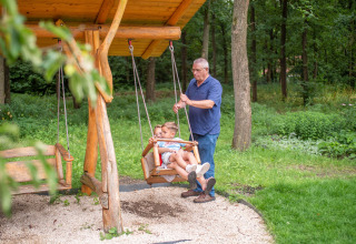 Een oudere man duwt twee kinderen op een houten schommel in Recreatiepark Beekbergen, Gelderland, Nederland.